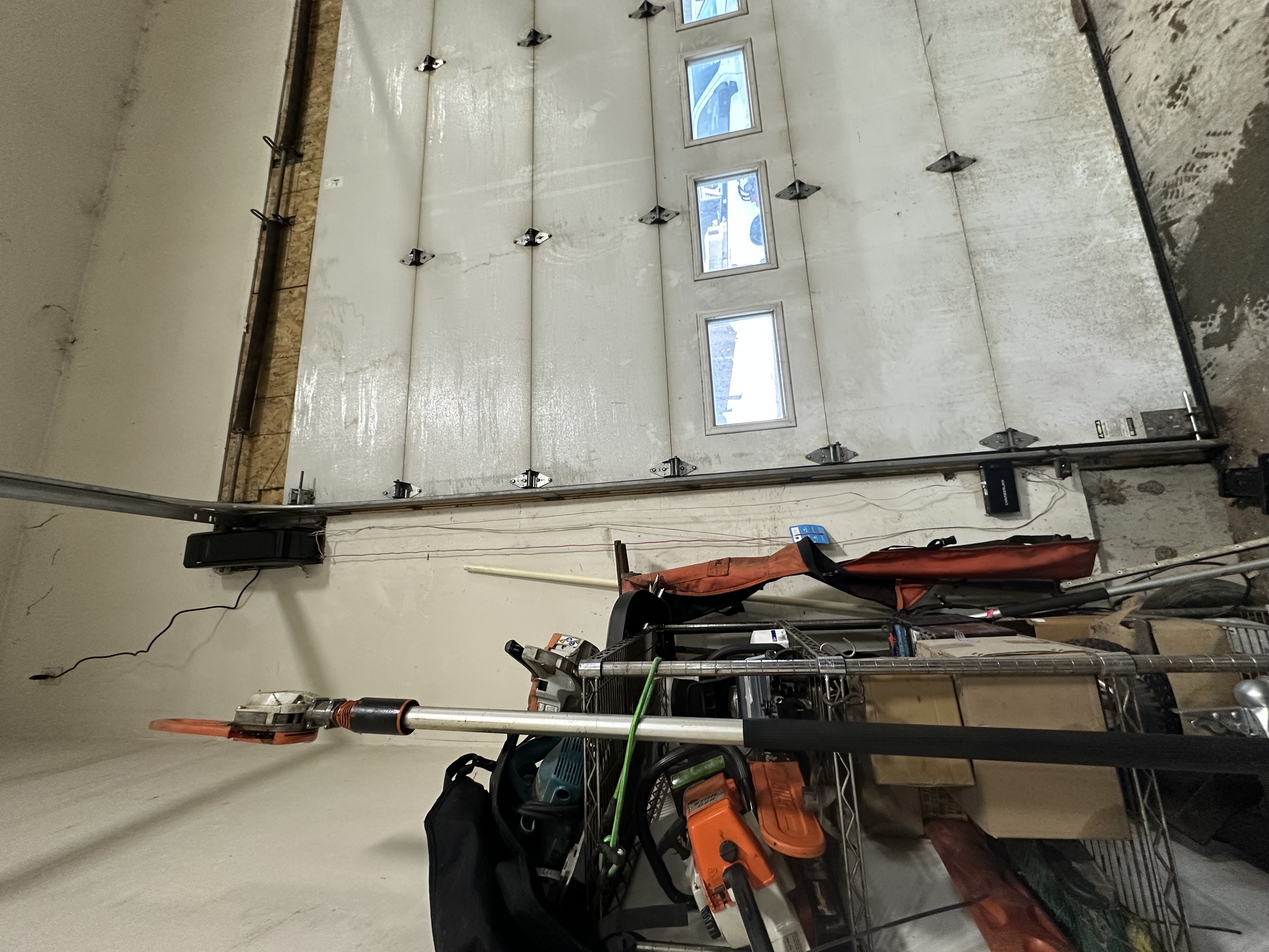 Garage door interior view showing track system, torsion spring, and professional repair tools on-site