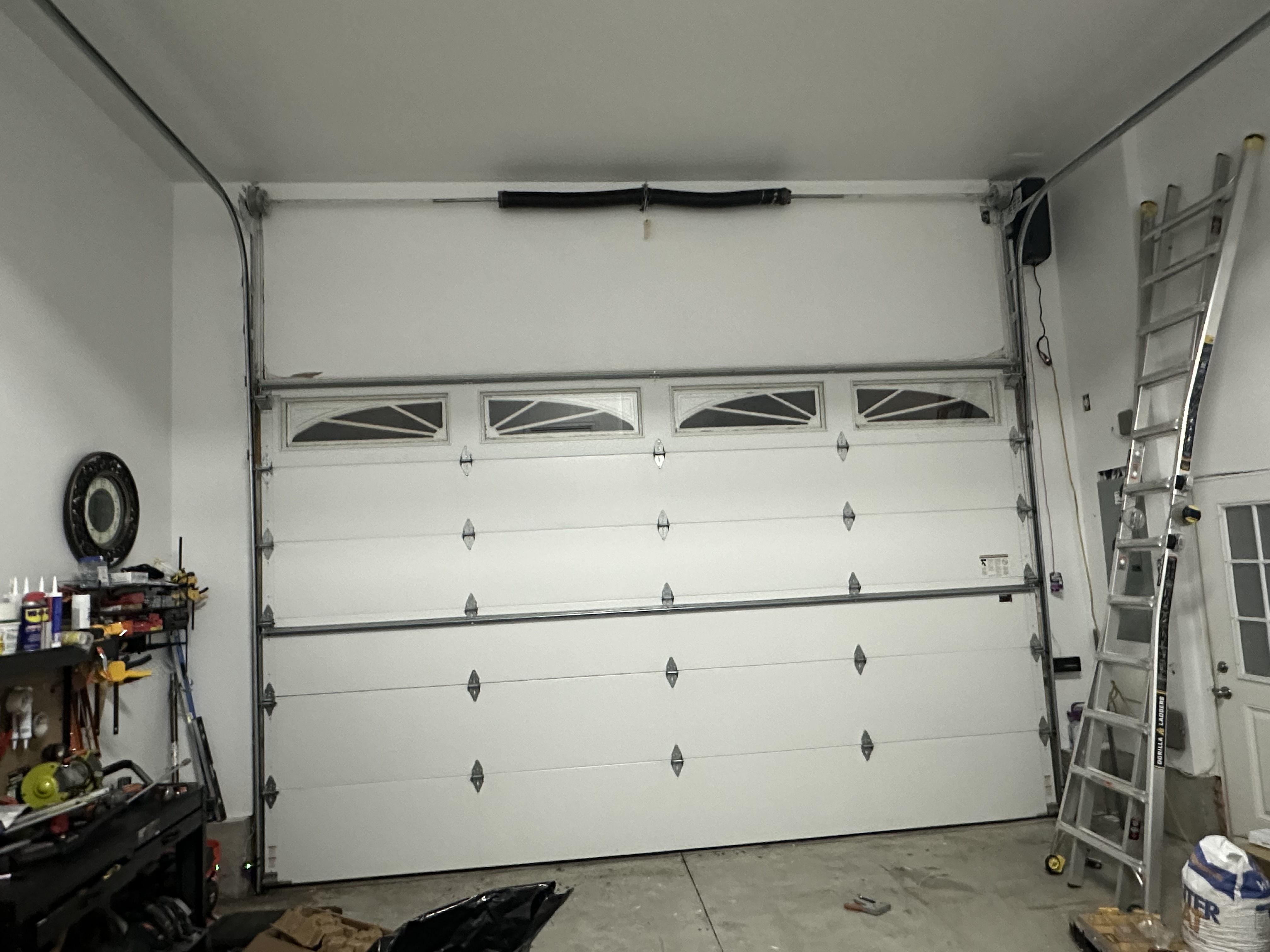 White residential garage door with decorative sunburst windows showing torsion spring and opener hardware